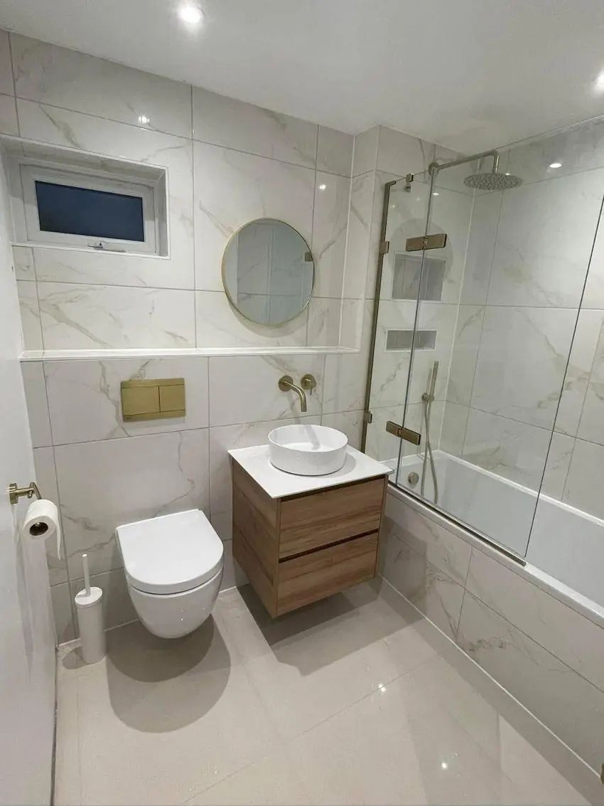 Bathroom after renovation — white marble tiling, wood vanity and brass fittings