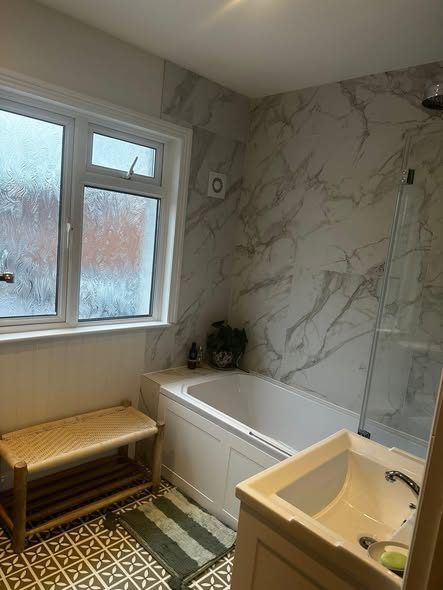 Finished bathroom with a marble bath surround beside a frosted sash window